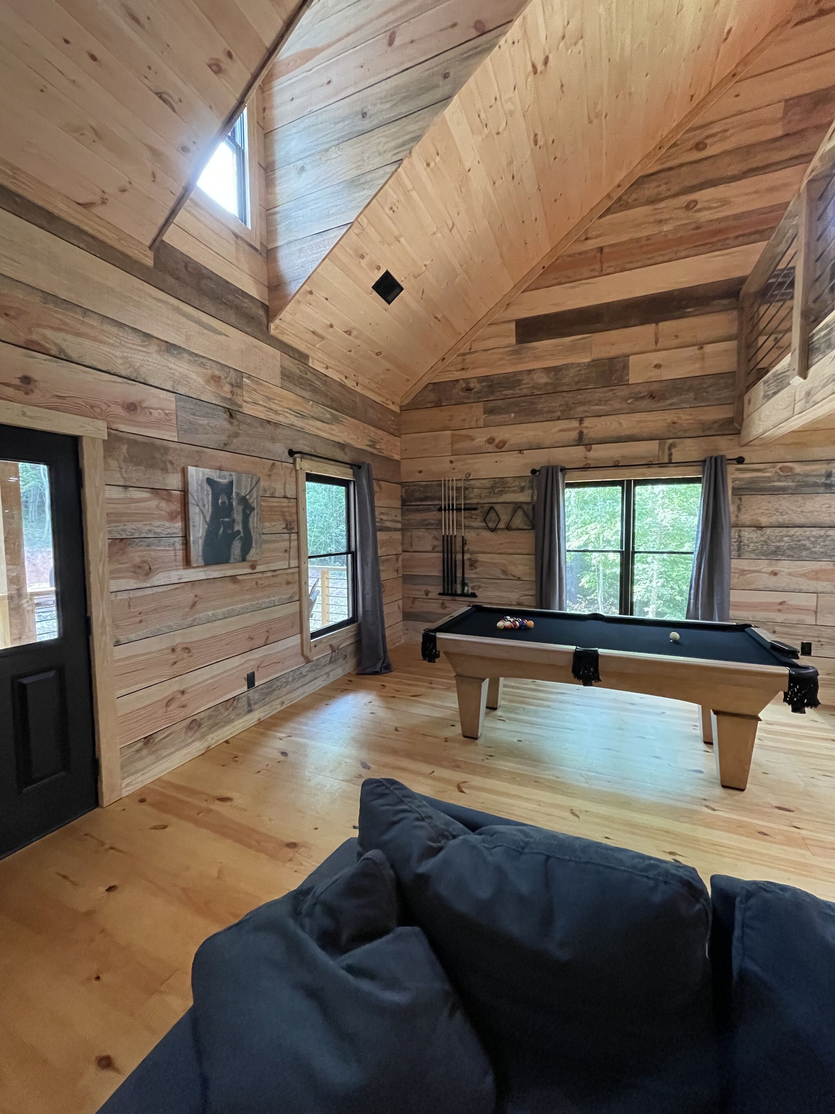 Un intérieur en bois avec une table de billard, un canapé et des fenêtres.