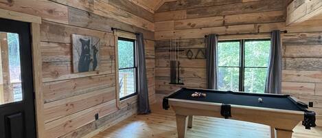Un intérieur en bois avec une table de billard, un canapé et des fenêtres.