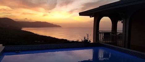 A swimming pool with a view of the ocean and a sunset.