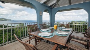 Comedor con una mesa lista para cuatro personas, con vistas panorámicas del océano y las colinas.