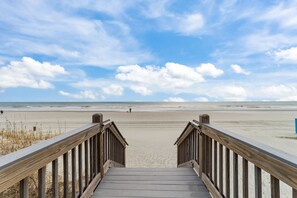A wooden staircase leading to a beach with a clear sky and a few people in the distance. - DISCOUNTED Dec 6th-27th Still Available! Oceanfront Condo STEPS FROM BEACH! (Myrtle Beach)