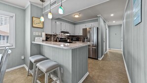Una cocina moderna con una isla central, taburetes de bar, electrodomésticos de acero inoxidable y vistas al salón.