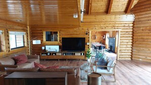 A log cabin interior with a wooden floor, a sofa, a TV, a dining area, and a fireplace. - Large Reunion Cabin By Lake And National Parks! (Panguitch)