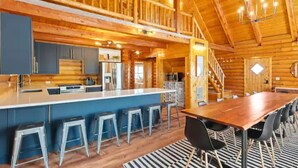 A spacious log cabin interior with a central island bar, multiple seating areas, and a staircase leading to an upper level. - Large Reunion Cabin By Lake And National Parks! (Panguitch)