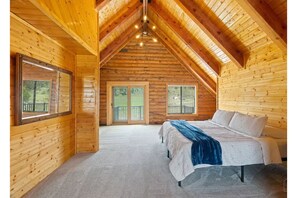 Un dormitorio tipo cabaña de madera con una cama grande, dos ventanas y un balcón.