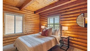 A log cabin bedroom with a bed, two windows, a bedside table with a lamp, and a mirror on the wall. - Large Reunion Cabin By Lake And National Parks! (Panguitch)