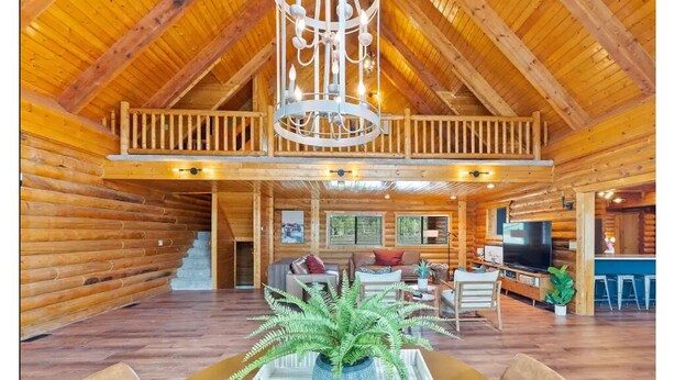 A spacious log cabin with a high ceiling, a balcony, a dining area with a table and chairs, and a living room with a sofa and television. - Large Reunion Cabin By Lake And National Parks! (Panguitch)