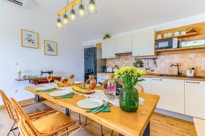 Une cuisine moderne avec des meubles en bois, une table à manger pour quatre personnes et un luminaire suspendu.