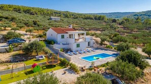 Uma casa de dois andares com piscina, rodeada por vegetação e colinas.