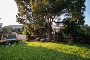 A well-maintained garden with a large tree, stone benches, and a clear pathway. - Sounio Panoramic Loft (Lavreotiki)