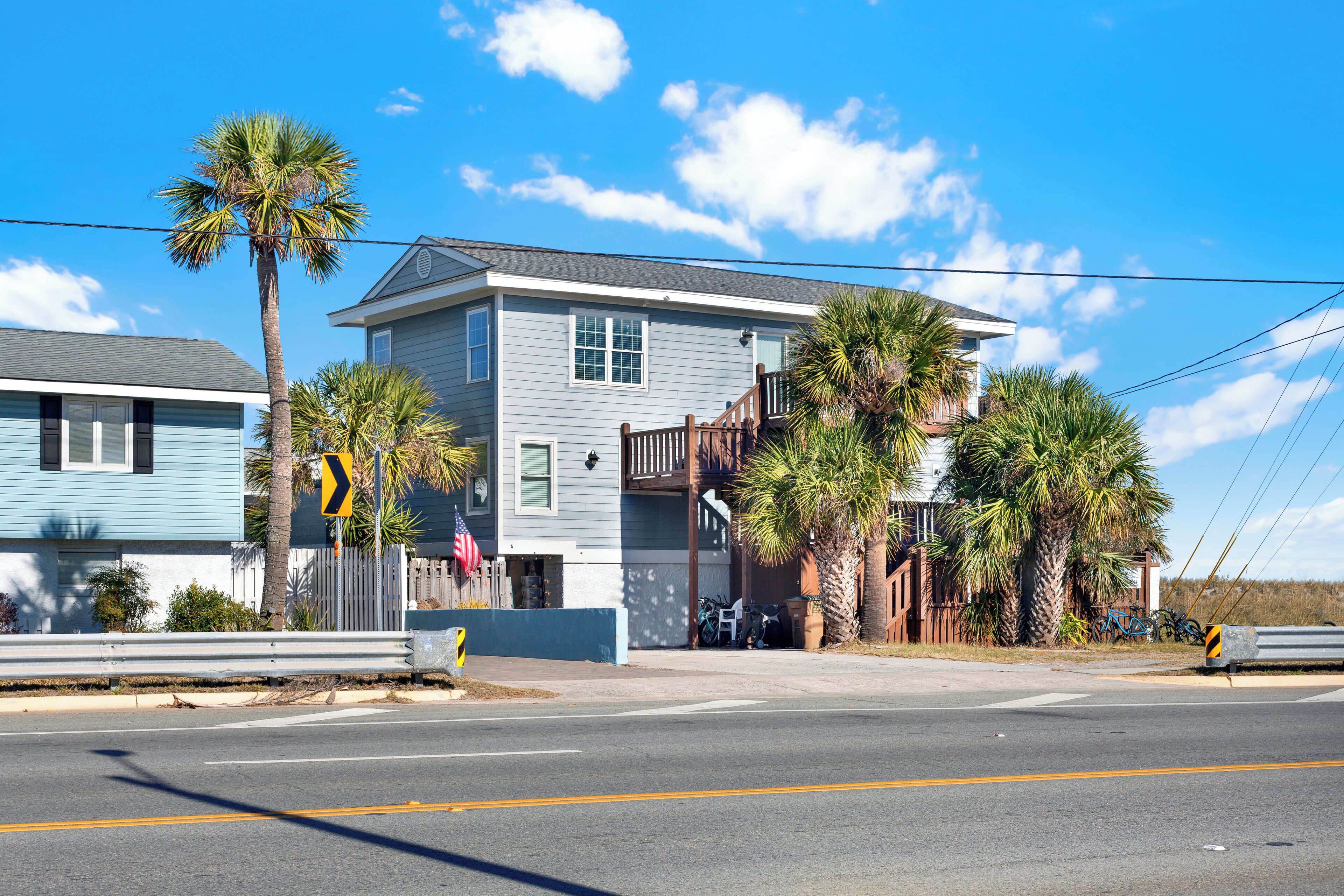 A two-story house with a balcony, a palm tree, and a bicycle parked outside.