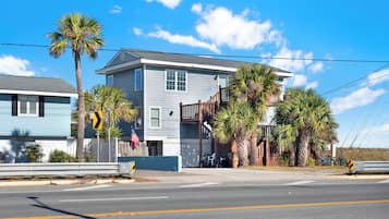 A two-story house with a balcony, a palm tree, and a bicycle parked outside.
