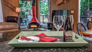 A dining area with a table set for two, a bottle of wine, and a fireplace. - Mystic Meadow ~ Sweet Cabin + Meadow Views (Shaver Lake)
