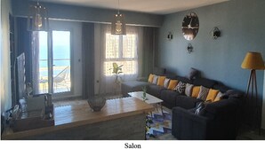 A living room with a sofa, coffee table, and a view of the sea. - Oran sea & bay apartment (Oran)