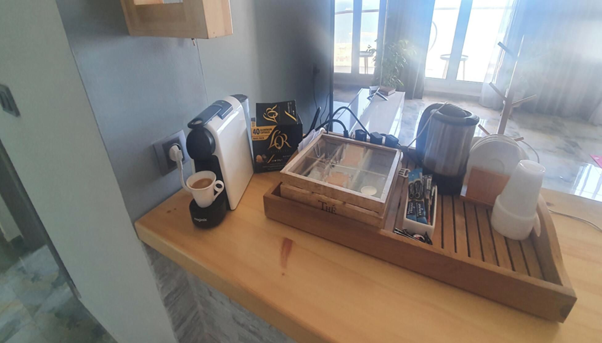 A wooden countertop with a coffee maker, a cup of coffee, a box of L'Or hair care products, a transparent box with items, and a white mug.