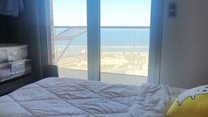 A room with a bed, a window with a view of a bridge and water, and a shelf with items. - Oran sea & bay apartment (Oran)