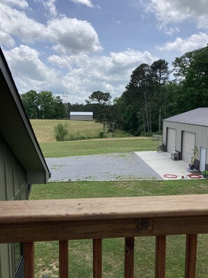 A view from a balcony overlooking a grassy yard with a building and trees.