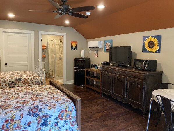 A bedroom with a bed, a dresser, a television, and a microwave.