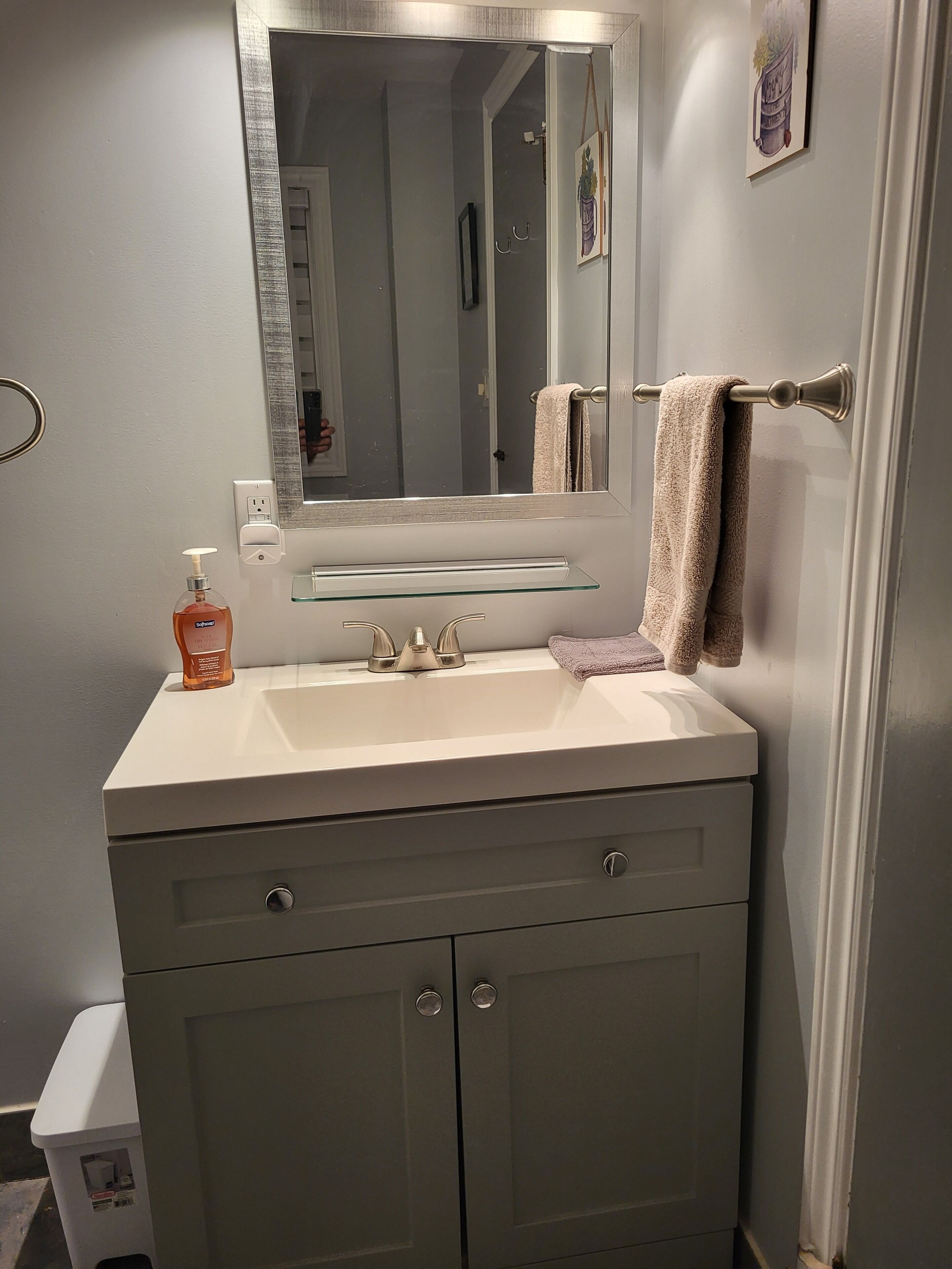 Une salle de bain avec un lavabo blanc, un miroir, un porte-serviettes et un distributeur de savon.