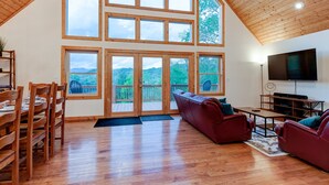 Un vaste salon doté d’un haut plafond, de grandes fenêtres, d’un plancher en bois, d’un canapé rouge, d’un téléviseur et d’un coin repas avec des chaises et une table en bois.