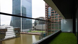 Blick von einem Balkon auf einen Fluss und moderne Gebäude im Hintergrund.