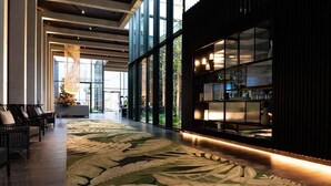 Eine geräumige Lobby mit großem floralem Teppich, einem modernen Empfangstresen und einer Glaswand mit Blick ins Freie.