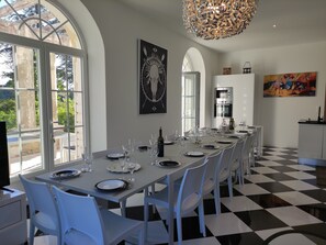 A dining area with a long table set for a meal, large windows, and a modern chandelier.
