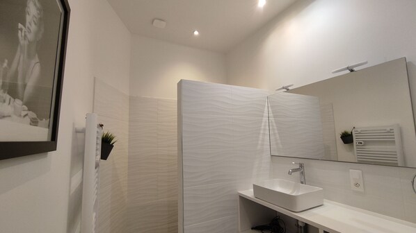 A modern bathroom with a large mirror, a white sink, and a shower area.