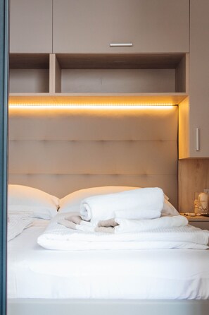 A neatly made bed with white linens and a rolled towel, a bedside table with a lamp, and a wall-mounted shelf above the bed. - Beachfront Sunset Villa (Brodarica)