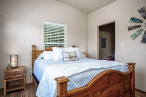 A bedroom with a wooden bed, a bedside table, a window with blinds, and a wall-mounted decoration.