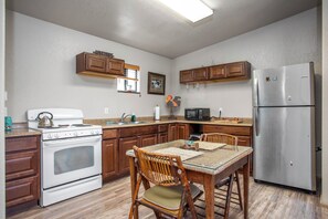 A kitchen with wooden cabinets, a stainless steel refrigerator, a stove, a microwave, and a dining table with chairs.