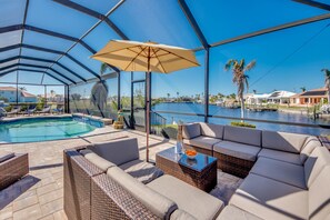 A covered outdoor area with a pool, wicker furniture, and a view of a body of water.