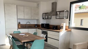 A modern kitchen with white cabinets, a wooden dining table, teal chairs, and a built-in oven. - 10 min from the beach and 5min from the town center (Propriano)