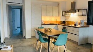 A modern kitchen with a dining area, featuring a wooden table and teal chairs, a built-in oven, and a coffee machine. - 10 min from the beach and 5min from the town center (Propriano)