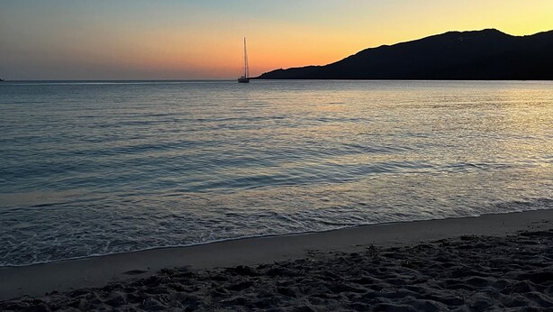 A beach with calm waters, a sailboat, and a distant mountain. - 10 min from the beach and 5min from the town center (Propriano)