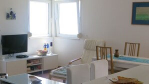 A living room with a television, a dining table, and a chair. There is a window with curtains, a ceiling fan, and a tiled floor. - The Bay Panoramic Views (5 min from the beach) - perfect for (Herceg Novi)
