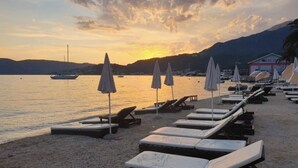 A beach with sun loungers and umbrellas, a boat on the water, and a mountain in the background. - The Bay Panoramic Views (5 min from the beach) - perfect for (Herceg Novi)
