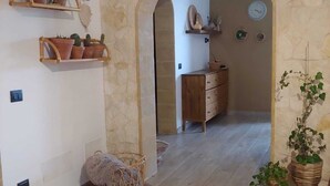A room with a stone archway, wooden furniture, and potted plants. - The First Flower (Noto)