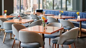 A restaurant interior with tables and chairs, a blue cushioned bench, and a vase with flowers on each table. - Lockwood Hotel (Waterville)
