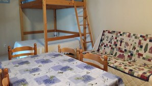 Kerrossänky, jossa on tikkaat, pöytä, jonka päällä on kukallinen pöytäliina, ja sohva, jossa on tikattu päällinen.