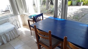 Ruokailutilassa on sininen pöytä ja puiset tuolit, valkoinen penkki sekä suuri ikkuna, josta avautuu näkymä puutarhaan.
