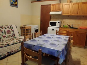 A compact kitchen with wooden cabinets, a microwave, a small oven, and a dining table with chairs.