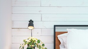 Une chambre avec un lit blanc, une table de chevet avec une lampe et une plante.