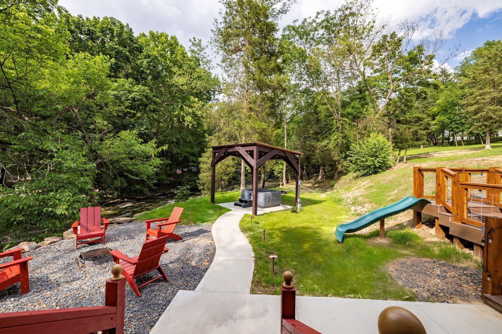 A covered outdoor seating area with a grill, red Adirondack chairs, and a slide.