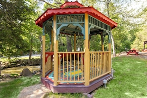 Ein Pavillon mit rotem Dach und farbigem Boden, umgeben von Gras und Bäumen.