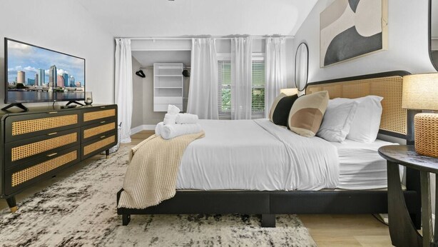 A modern hotel bedroom with a bed, a television, a wardrobe, and a view of the city.