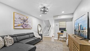 A modern living room with a grey leather sofa, a flat-screen TV, and a staircase leading to an upper level.