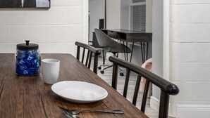 Una mesa de comedor con un plato blanco, dos tenedores, una taza blanca y un recipiente con objetos azules.