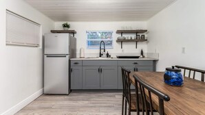 Una cocina compacta con gabinetes grises, un refrigerador blanco y una mesa de comedor de madera con sillas.