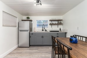 Compact kitchen with refrigerator, sink, and window above the sink. Dining area with table and chairs.